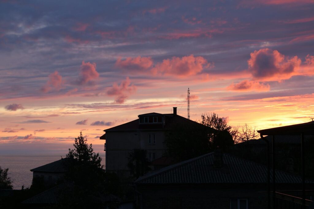 Traumhafter Sonnenuntergang über dem Meer mit Silhouetten von Häusern, symbolisiert Entspannung und Balance nach der Arbeit.