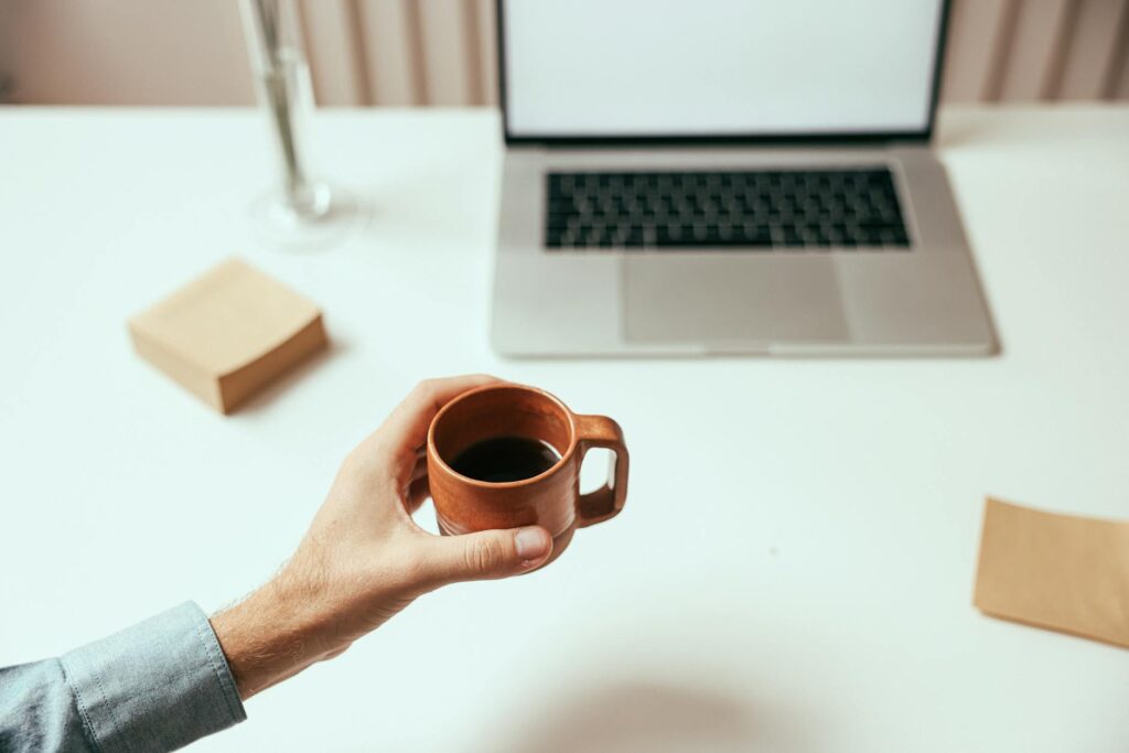 Frau hält Kaffeetasse am Schreibtisch mit Laptop, symbolisiert Work-Life-Balance und bewusste Arbeitspausen