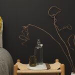 Entspannendes Schlafzimmer mit gelben Kissen, grauem Sessel, Duftflasche und trockenen Pflanzen vor dunkler Wand