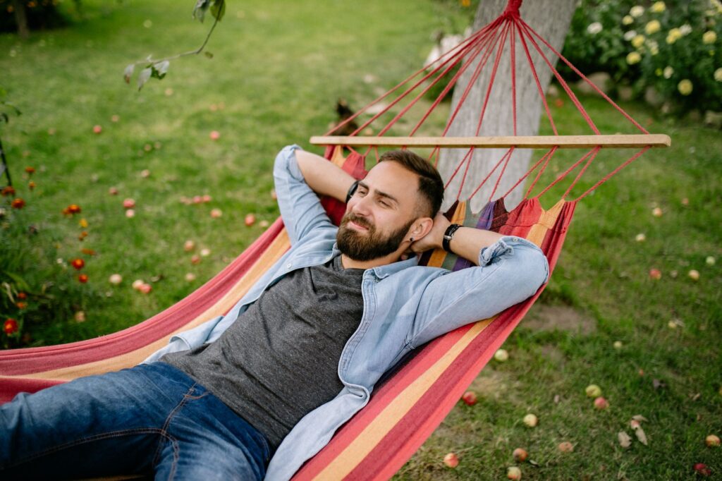 Mann entspannt sich in rot-gelber Hängematte im Garten und setzt sich Zeit für Wellness und Erholung zur Priorität