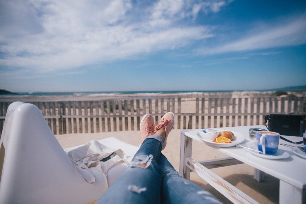 Person entspannt auf Strandterrasse mit Frühstück, Blick auf Meer und Dünen, ideale Wellness-Auszeit zum Abschalten